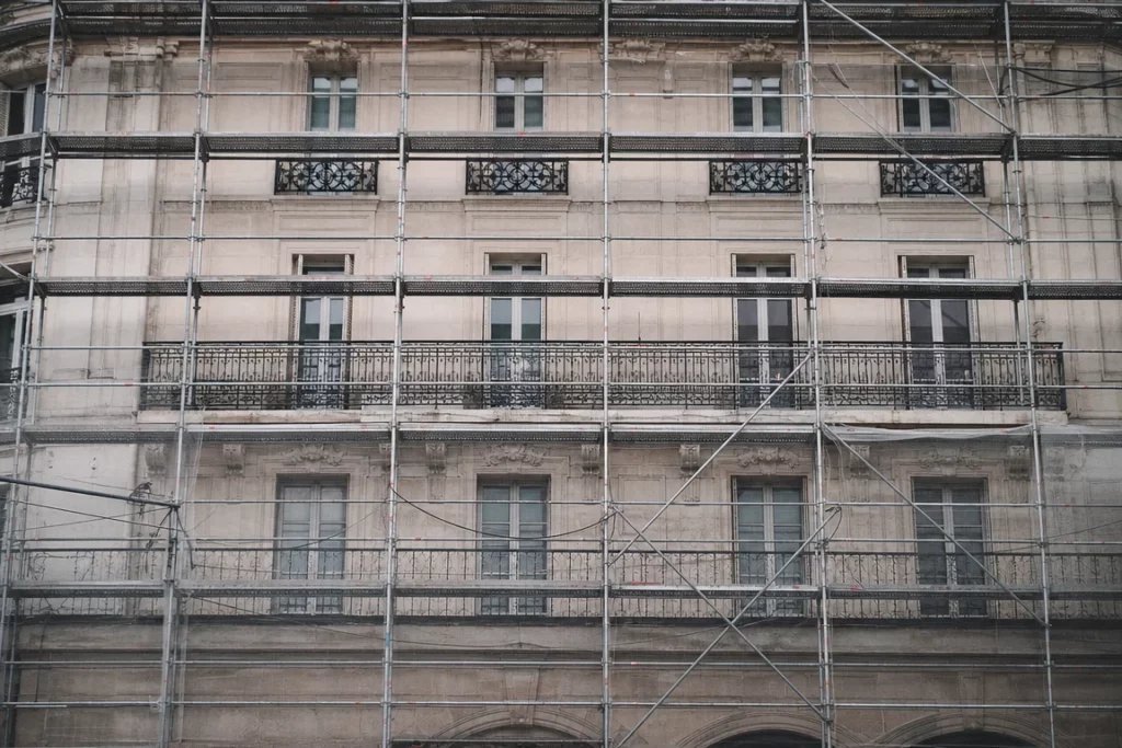 Façade générique d’un hôtel parisien haussmannien sous échafaudage en cours de rénovation, lumière douce sur pierre et métal