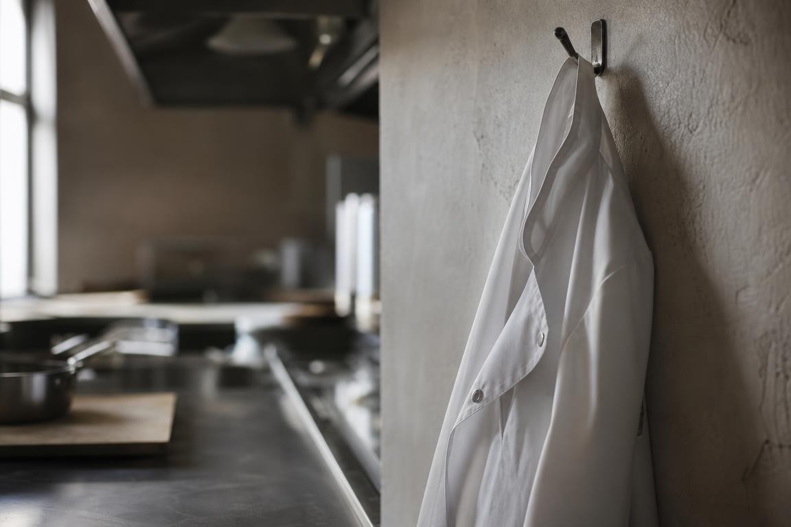 Scène évocatrice de départ d’un chef : une veste de chef blanche suspendue dans une cuisine professionnelle générique