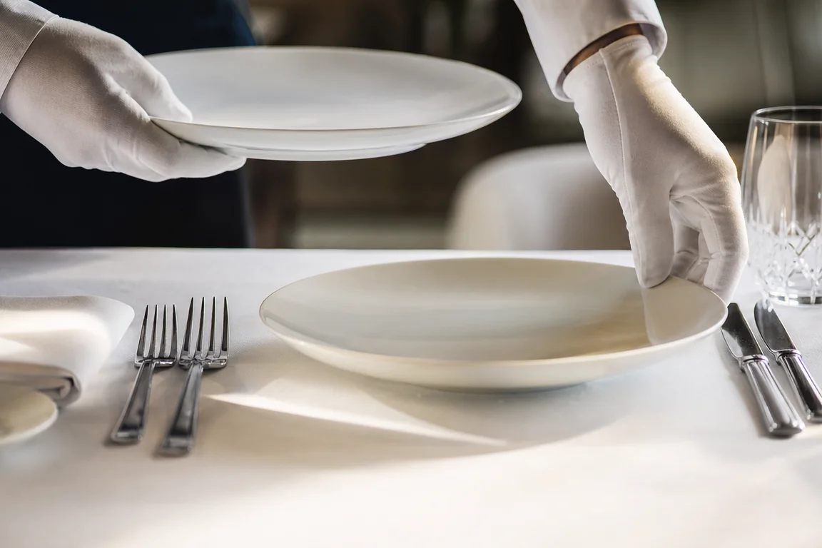 Mains gantées échangeant deux assiettes sur une table gastronomique immaculée