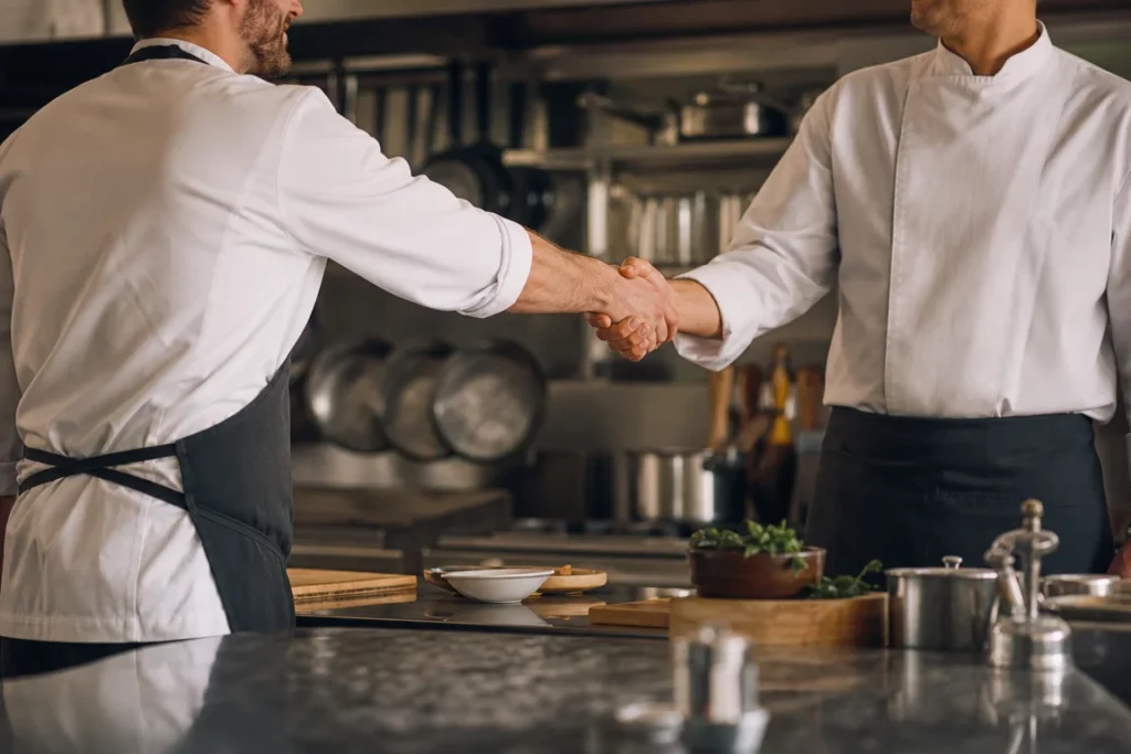 Scène évocatrice de recrutement en cuisine : deux cuisiniers anonymes se serrent la main dans un décor professionnel générique.