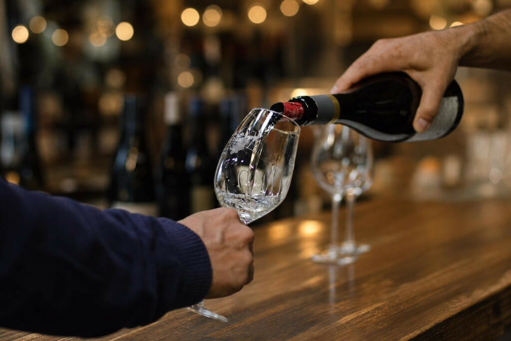 Verre à vin élégant vide sur un comptoir en bois avec bokeh chaleureux en arrière-plan, évocation d’un salon des vins familial